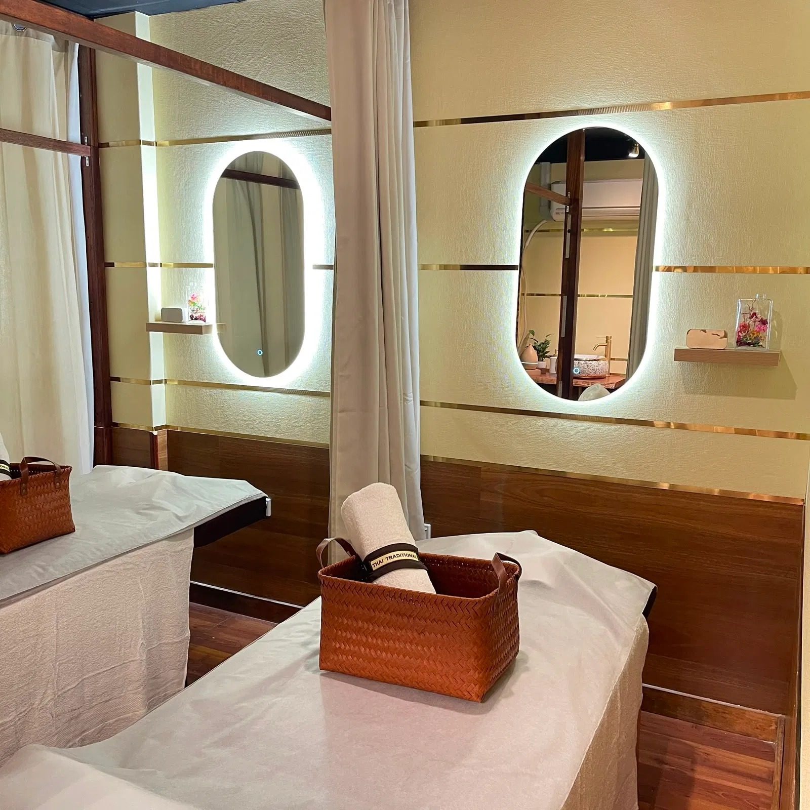 A treatment room at Thai Traditional Massage: cream walls, brass trim, oval mirrors and a rolled towel in a woven basket